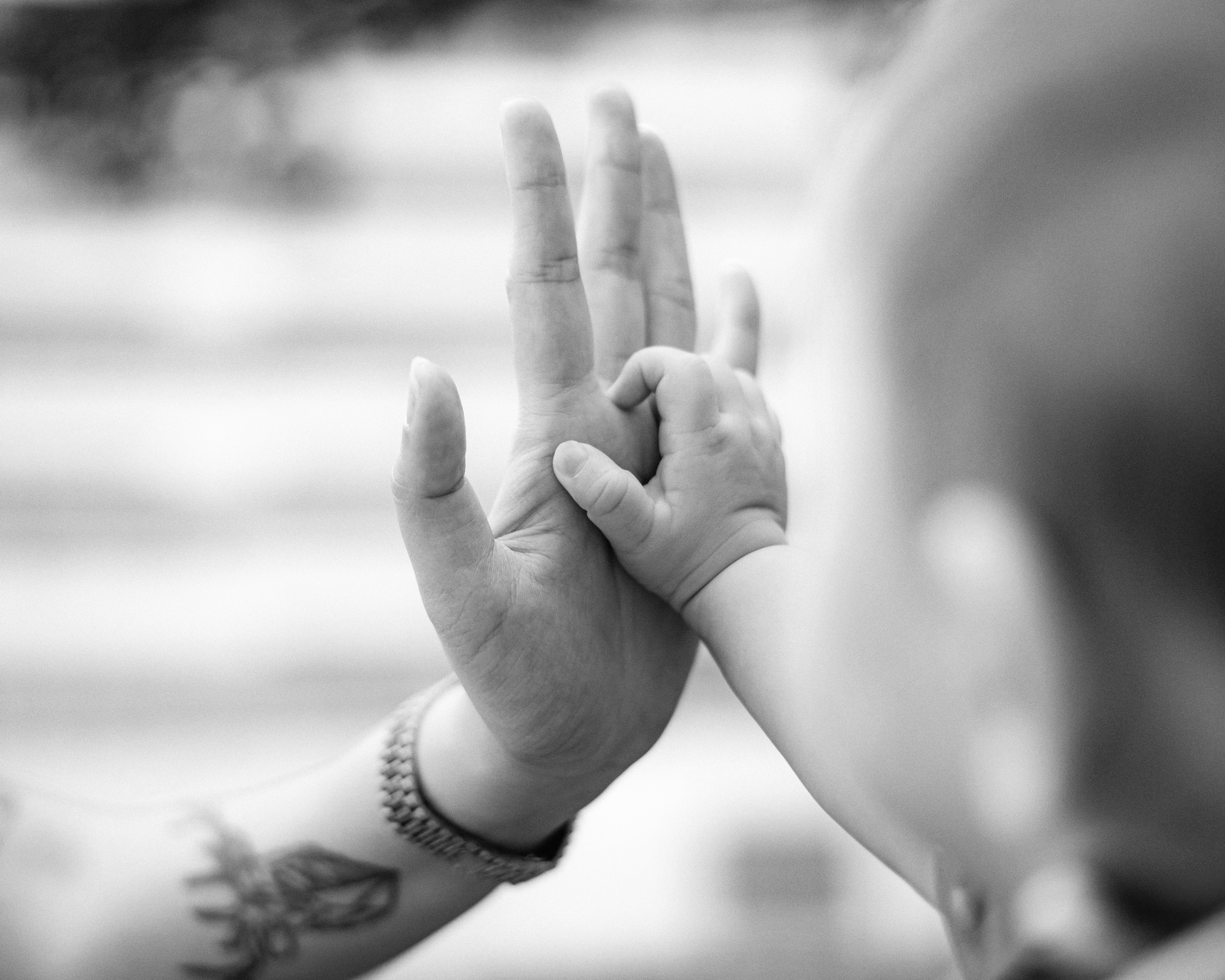 A parent's hand cradles a newborn baby's foot in soft window light.